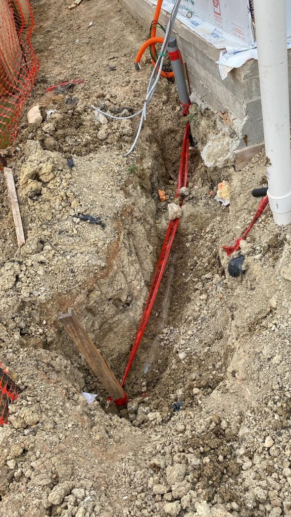 Construction site with dug trench some pipes and red tape.