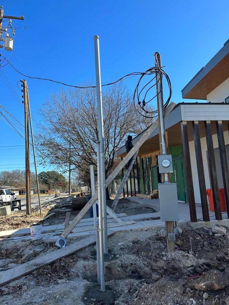 Electrician on a ladder working on building under construction and exterior electrical wiring with a meter.