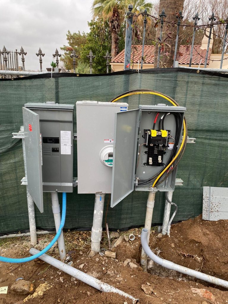 Three gray electrical panels, including a meter box, mounted on poles with conduit and wiring connections.