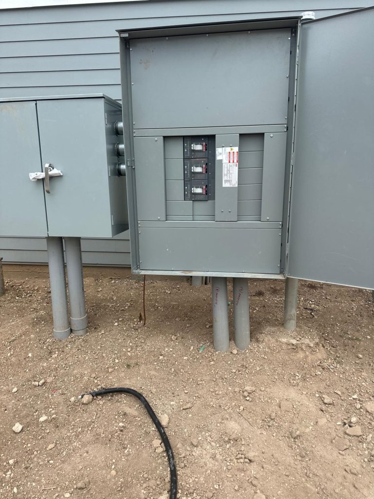 Two gray electrical panels mounted on poles, one open with visible circuit breakers.