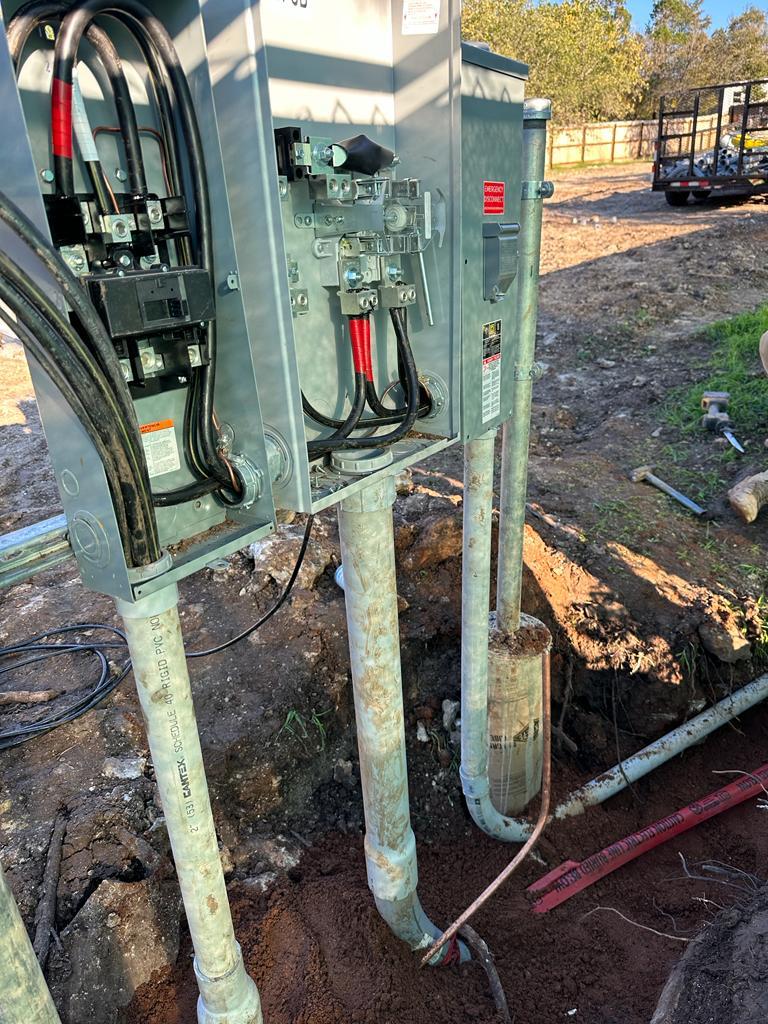 Outdoor electrical service panel with visible wires and breakers, connected to metal conduit running underground.