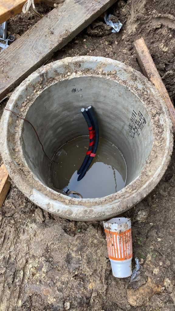 Underground 18 inches concrete manhole with three black electrical conduits bundled together and water pooled at the bottom.