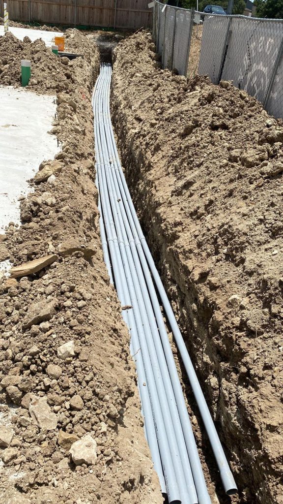 Long and narrow trench filled with gray pipes for underground electrical wiring.