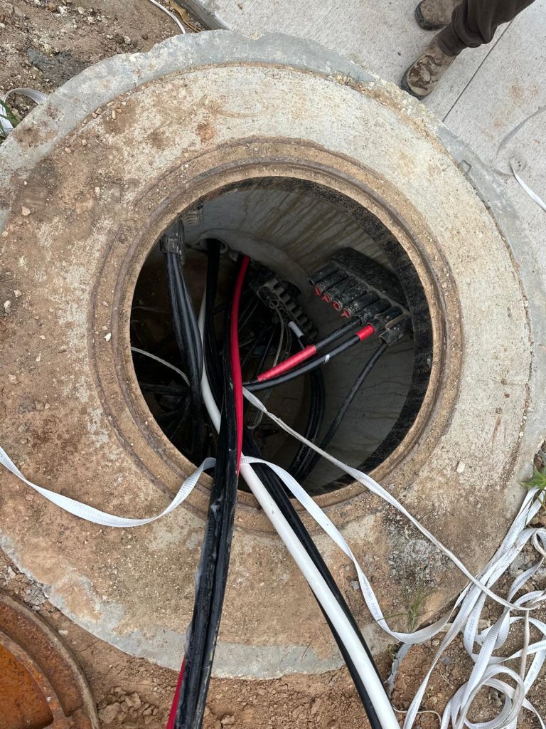 Open manhole revealing various electrical cables and a junction box with multiple connections.