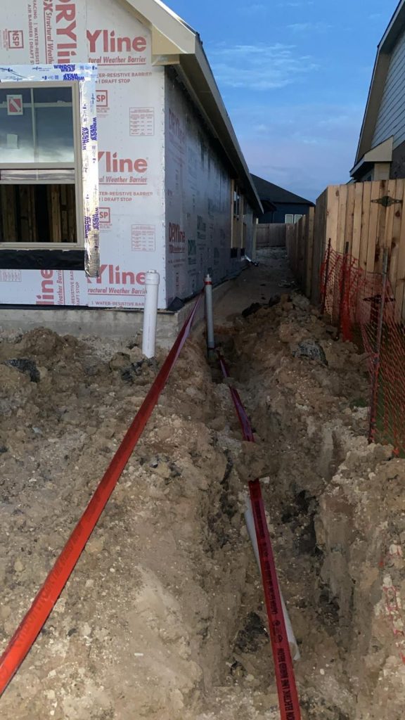 House under construction with trench dug for utility line next to it.
