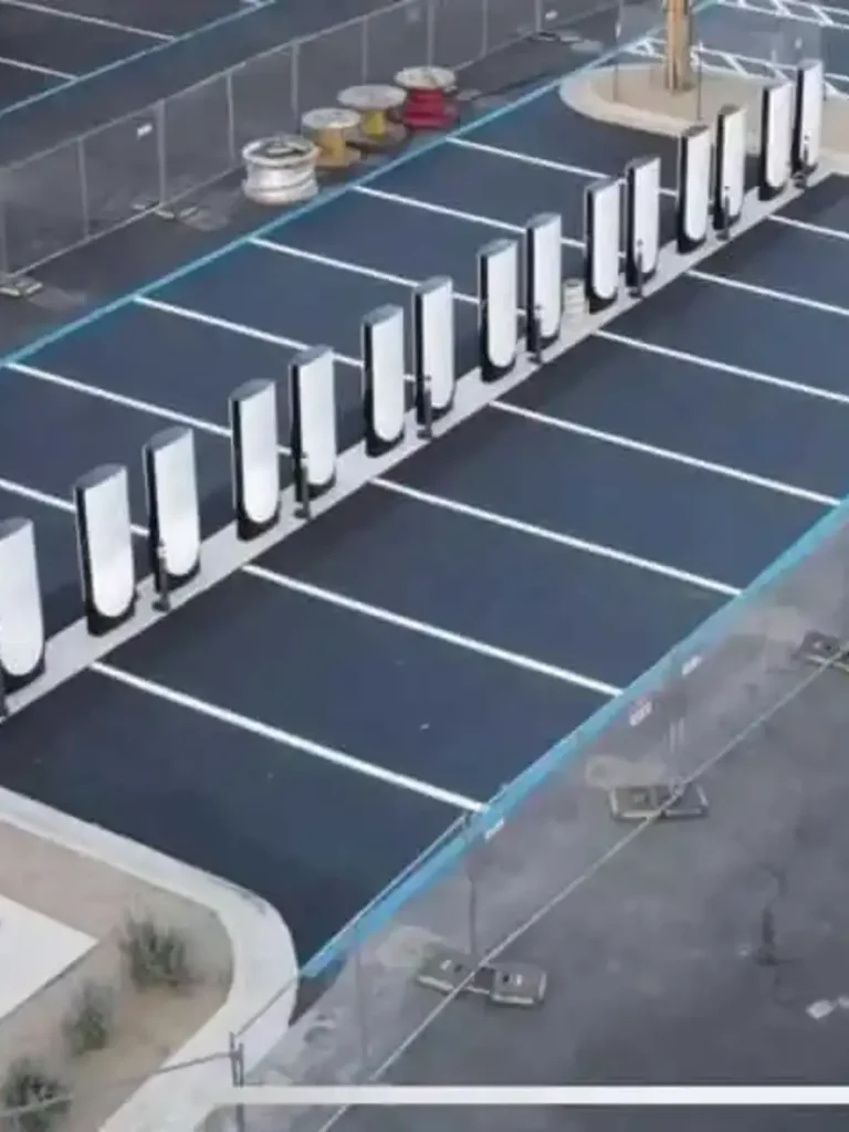 Drone aerial view of a complete Tesla Supercharger station in a large commercial parking lot, showing blue-painted spaces and multiple units in Austin by Soga Underground.
