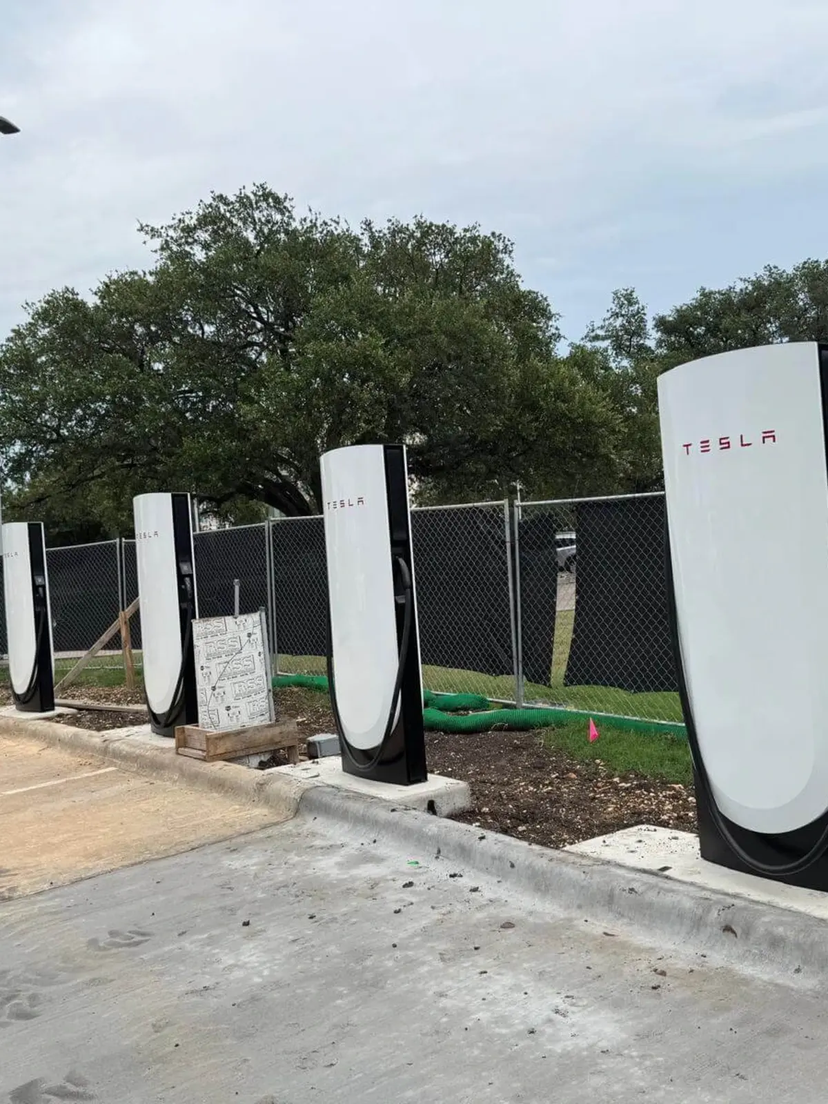 Row of multiple Tesla Supercharger stations under installation at a commercial site by Soga Underground, featuring a safety fence and concrete work.