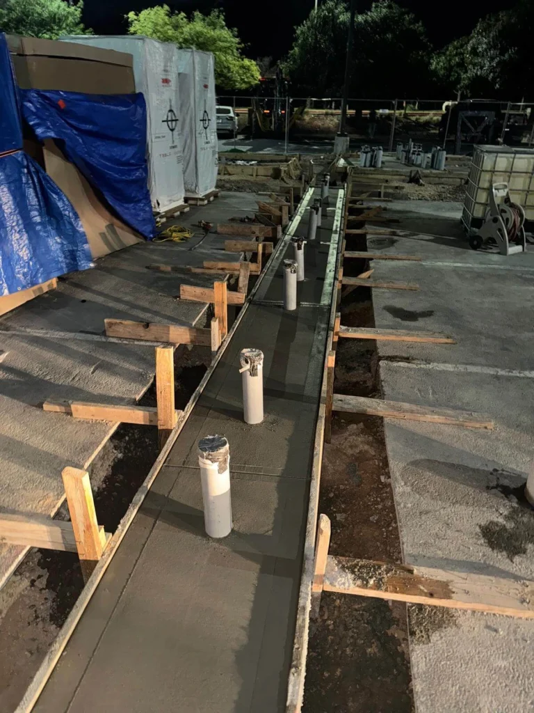Freshly poured concrete foundation with multiple PVC conduit risers for a row of new Tesla Supercharger units by Soga Underground
