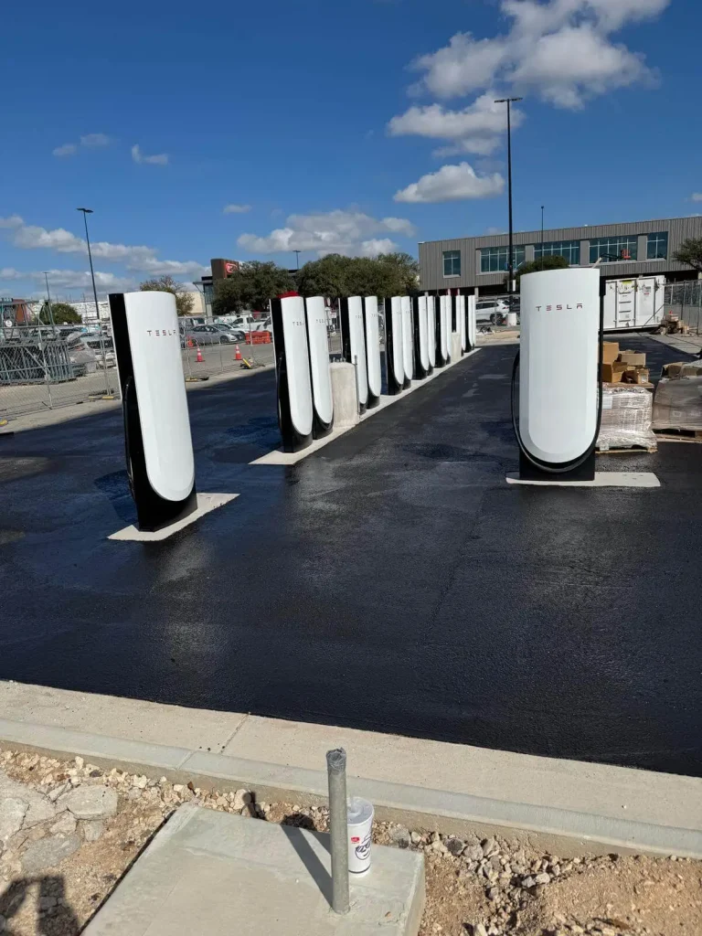 Row of Tesla Supercharger pedestals on fresh black asphalt at a commercial site, showcasing completed utility work in Austin by Soga Underground.