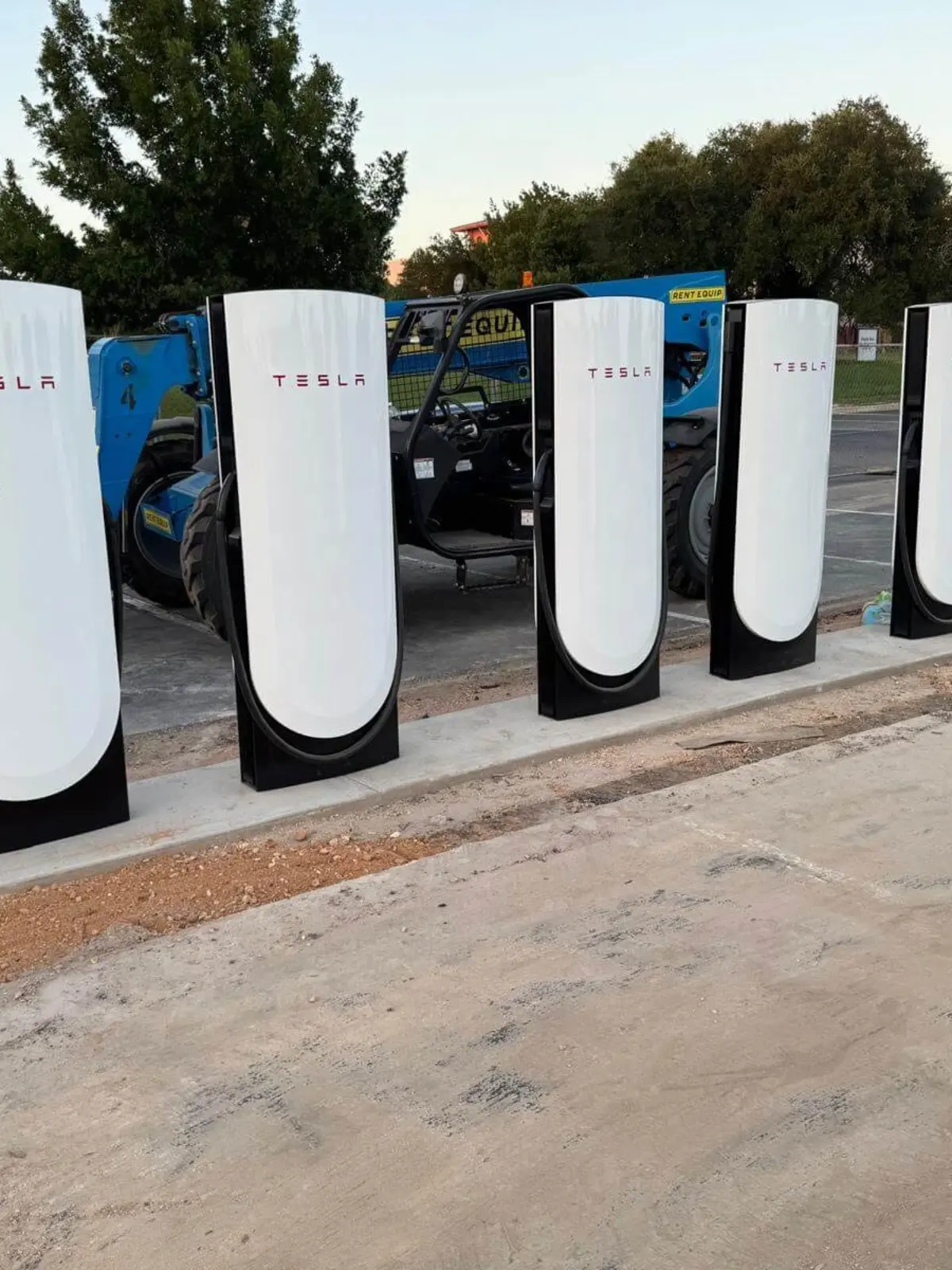 Row of newly installed Tesla Supercharger stations with a blue forklift in the background at a commercial construction site in Austin by Soga Underground.