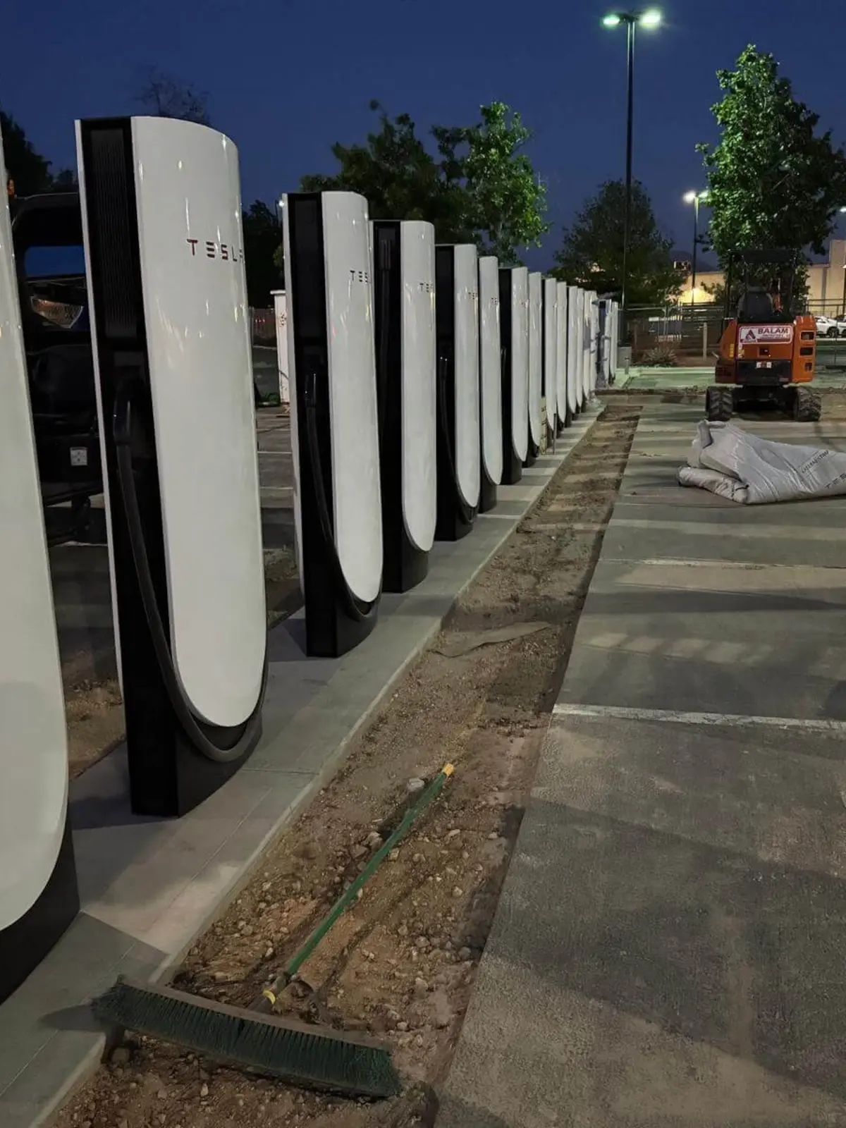 A long row of illuminated Tesla Supercharger stations at night in a clean commercial parking lot, demonstrating a completed installation project by Soga Underground.